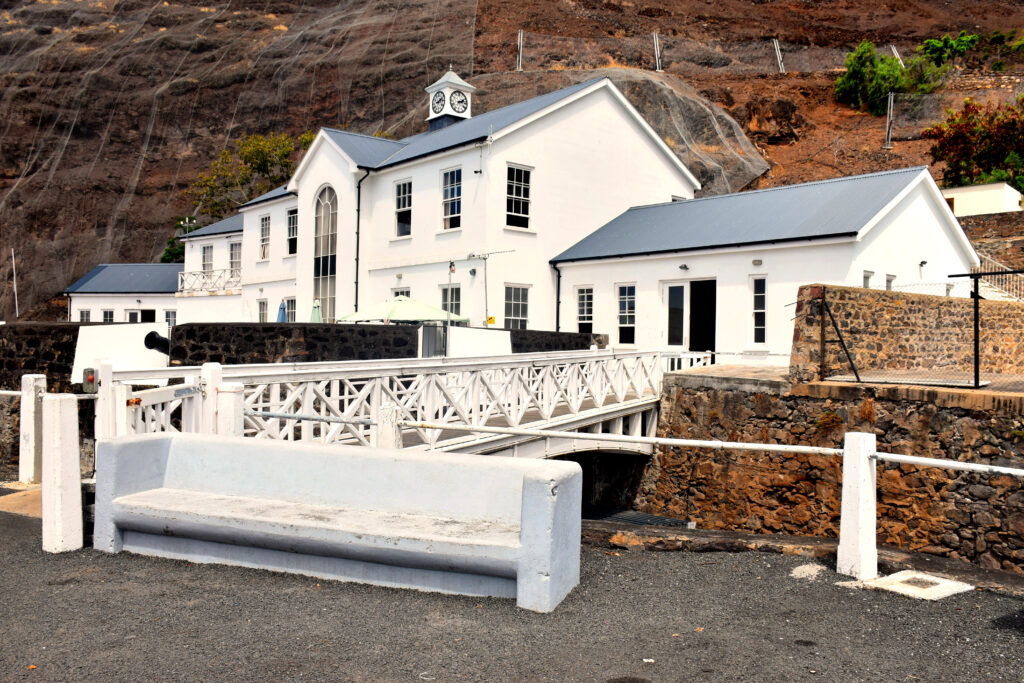 White colonial-style building with a clock tower, stone walls, and a small white bridge in front.