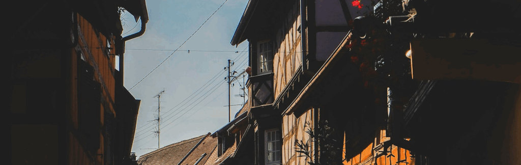 Narrow street with traditional wooden houses, flower boxes, and power lines under a clear sky.