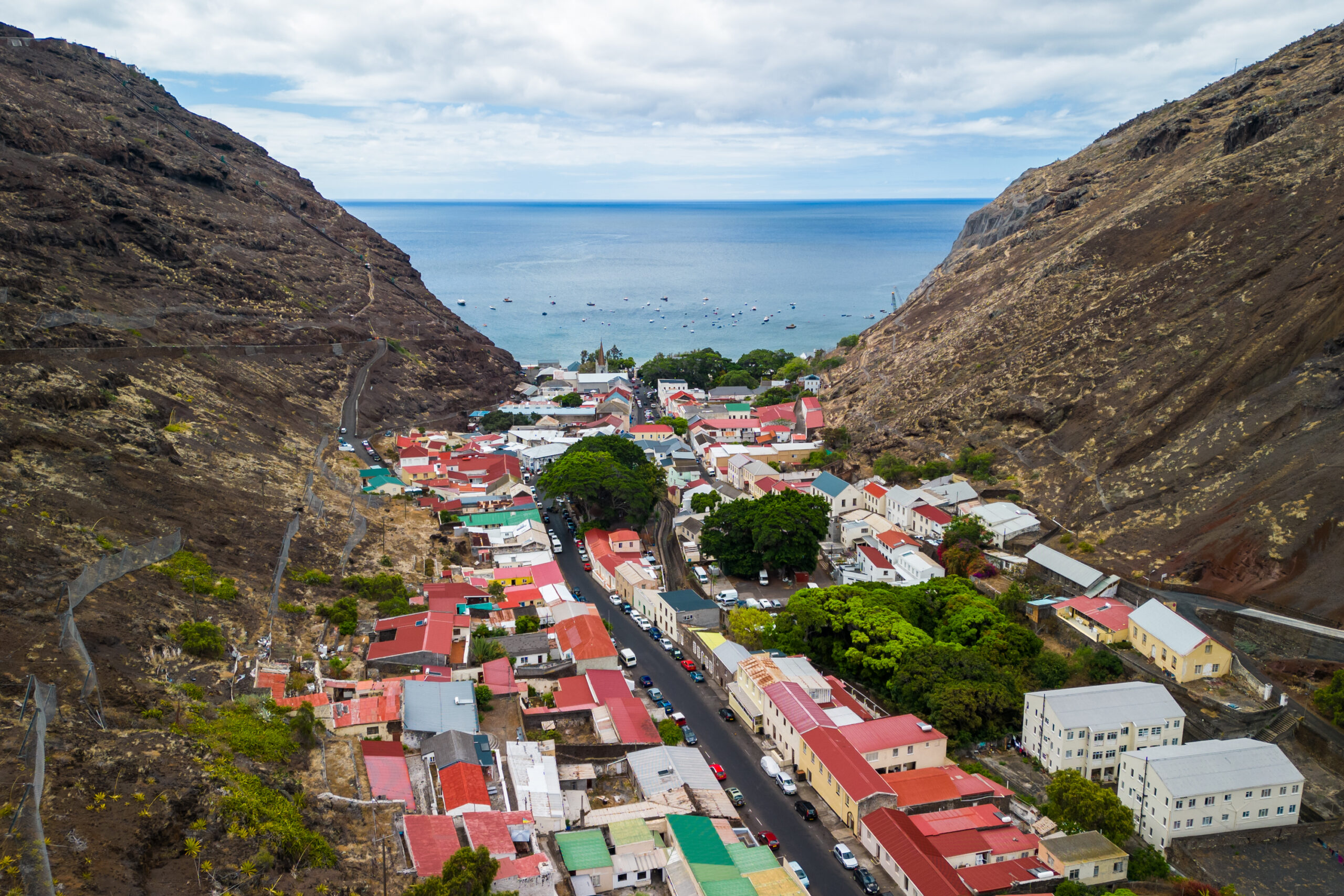 A coastal town with colourful rooftops nestled between rocky hills, overlooking boats on the blue sea.