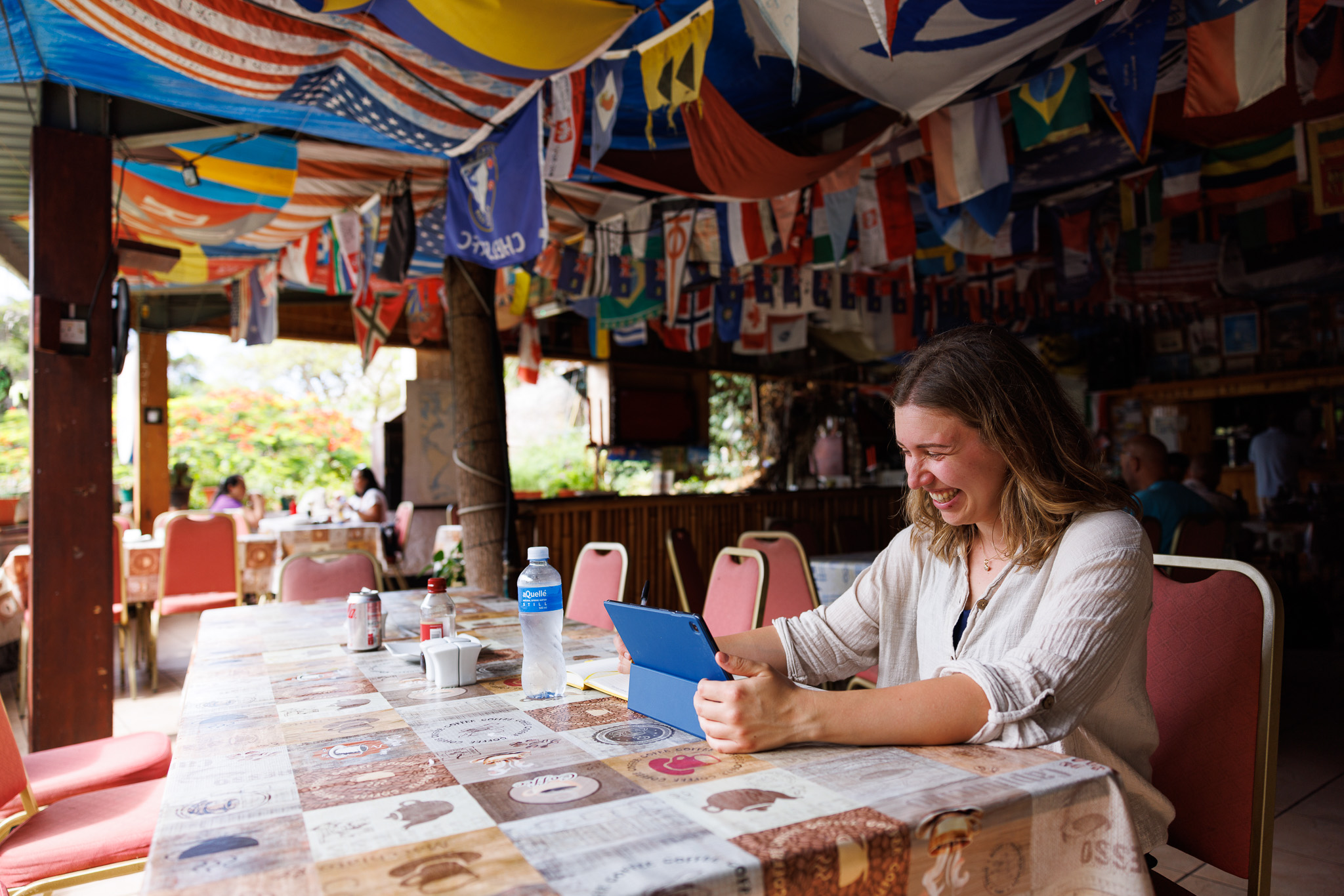 Woman smiling at a tablet in a colourful café decorated with flags from around the world.